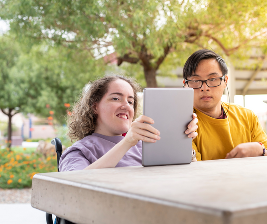 A young woman and man with disabilities look at a tablet device and provide user testing on accessibility and usability.