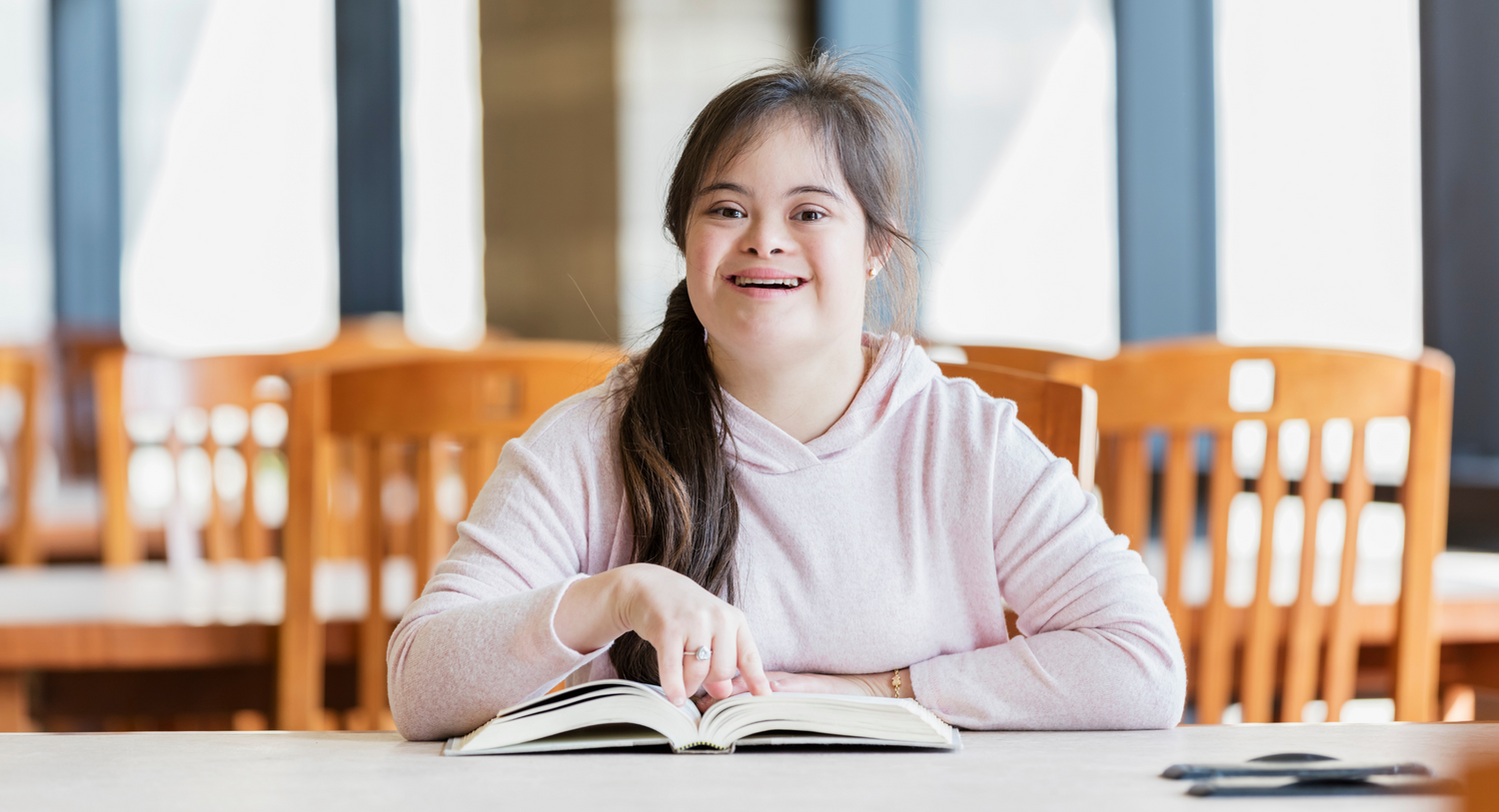 A young woman with intellectual disability smiling and reading an easy read page